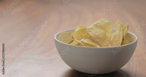 white bowl with black pepper seasoned potato chips on walnut wood table with copy space