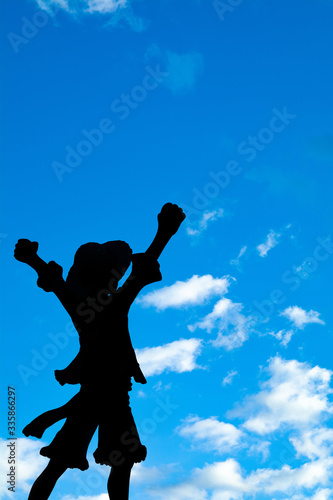 Silhouette of person at sunset celebrating a triumph with blue sky in the background. silhouette of person with arms raised to heaven. silhouette of a person with a straw hat.