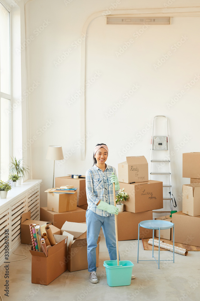 Vertical full length portrait of young Asian woman cleaning new house or apartment while looking at camera and smiling cheerfully, copy space Vertical full length portrait of young Asian woman cleaning new house or apartment while looking at camera and smiling cheerfully, copy space