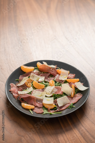 Salad with prosciutto, tangerines and vintage cheese on walnut table with copy space