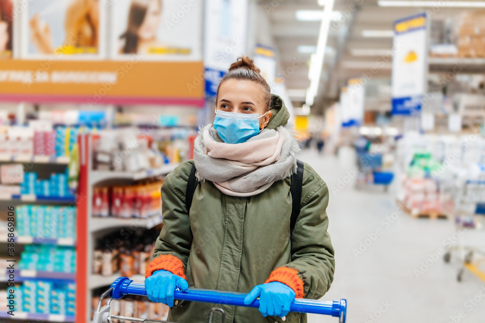 Obraz premium woman in medical gloves and mask in a supermarket with a trolley