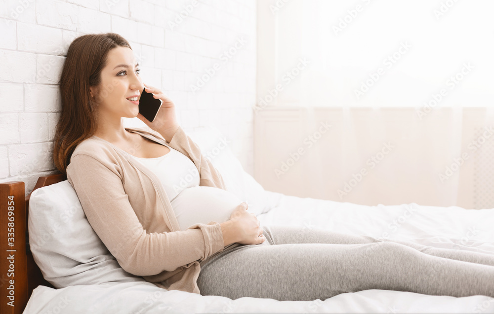 Cute pregnant woman talking on phone, lying in bed at home Cute pregnant woman talking on phone, lying in bed at home
