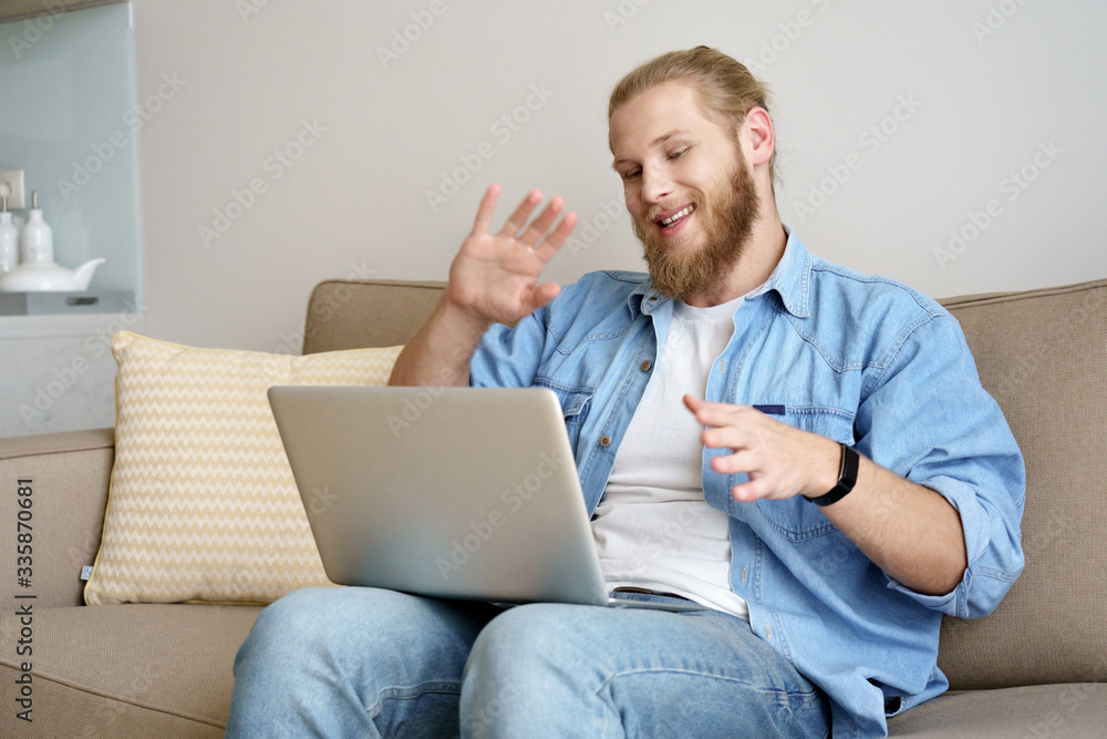 Happy young man waving hand video calling on laptop sitting on sofa working studying from home remote office. Smiling male distance worker student doing online conference webcam chat on computer. Happy young man waving hand video calling on laptop sitting on sofa working studying from home remote office. Smiling male distance worker student doing online conference webcam chat on computer.
