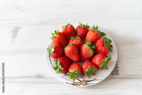 Fresh strawberries on a white plate on a soft wooden base