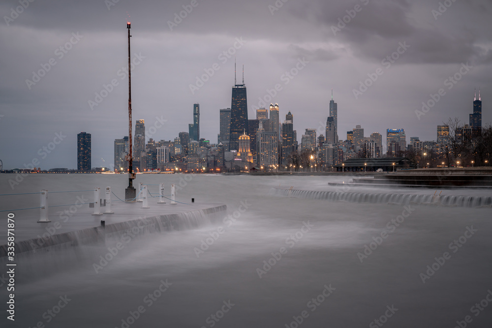 Obraz premium Fantastic cityscape panoramic skyline view of Chicago from Fullerton Avenue during a windy day with water cascading over a concrete pier at night just after sunset as lights begin to turn on in city.