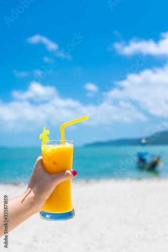 First-person view. Girl holds a glass cup of cold mango fresh on the background of a sandy tropical beach. White sand and a boat. Fairytale vacation in Thailand