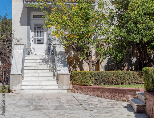 yard with trees and marble stairs to vintage house entrance white door © Dimitrios