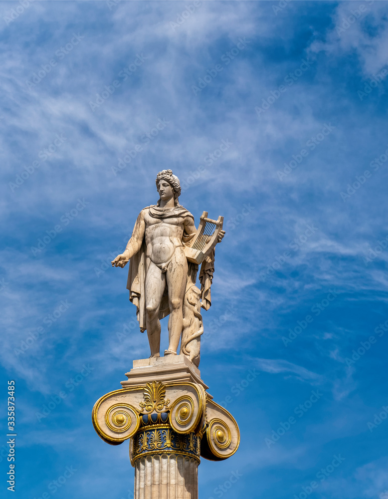 Apollo white marble statue on Ionian style column under blue sky with some clouds, Athens Greece Apollo white marble statue on Ionian style column under blue sky with some clouds, Athens Greece