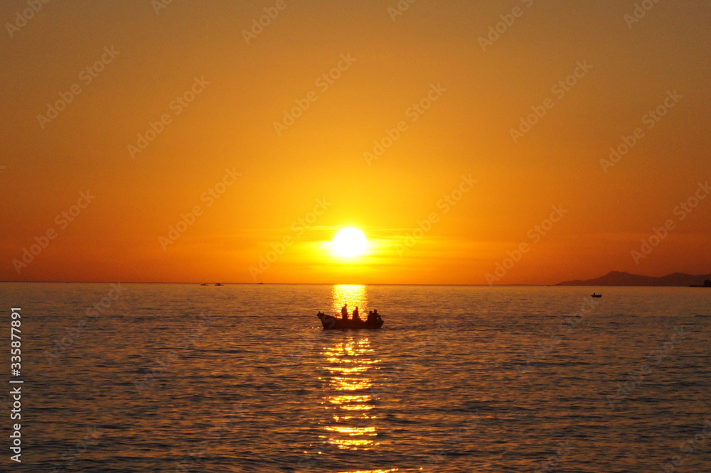 Sunset on the Marmara Sea with the silhouette of men on the boat and sun reflection on the water.