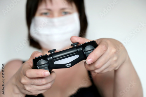Girl gamer in medical mask with gamepad playing video games. Joystick in female hands close-up, gaming addiction concept, home leisure at quarantine during covid-19 coronavirus pandemic