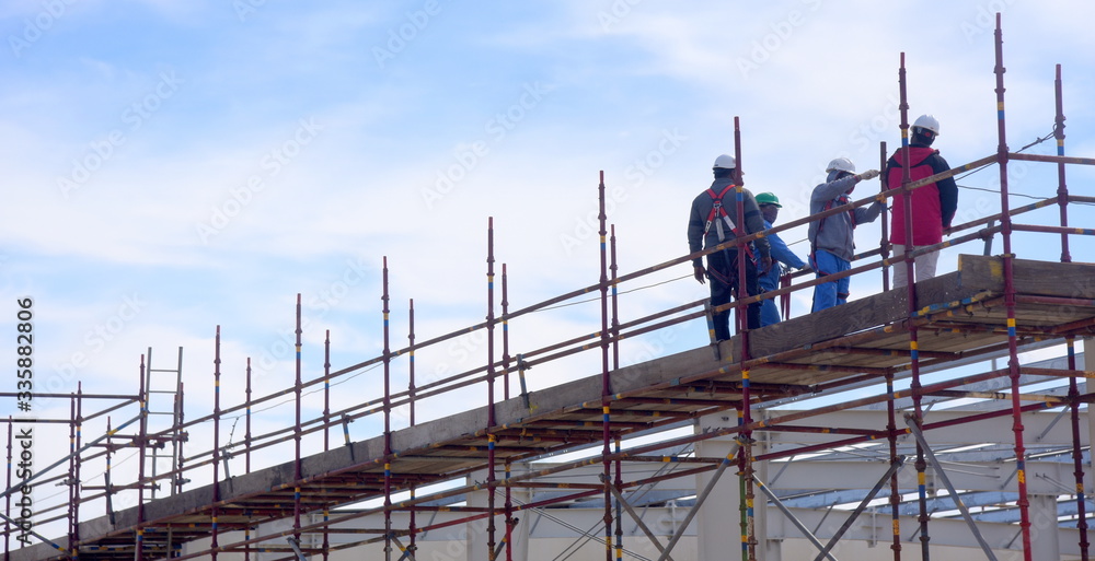 Bauarbeiter auf dem Gerüst einer Baustelle vor blauem Himmel Bauarbeiter auf dem Gerüst einer Baustelle vor blauem Himmel