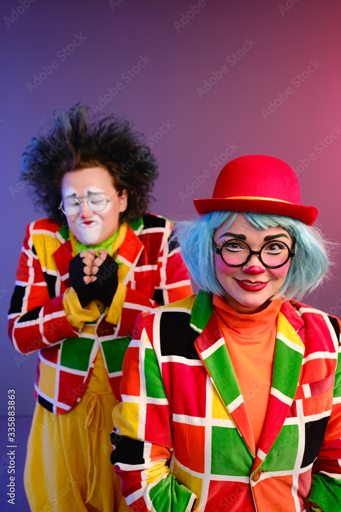 Two clowns a man and a woman with makeup in bright colored costumes are fooling around and showing a presentation