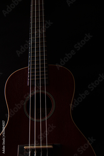 Ukulele brown wood grain in dark light for playing on black background.