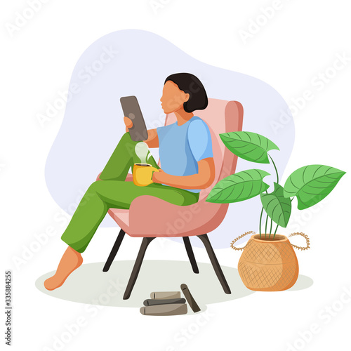 Pretty girl sitting in comfy armchair with a tablet and cup of coffee.