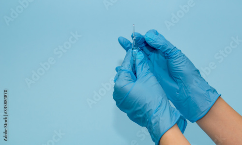 the medic's hands in blue gloves on a blue background open the vial