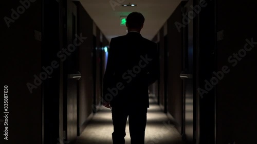 A man in a blue business suit is walking along the corridor of a hotel, shooting from the back, dim lighting, slow motion