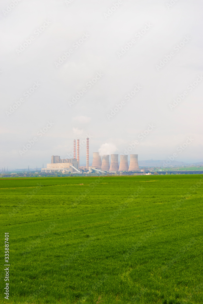 Nuclear power plant with green field and big blue clouds