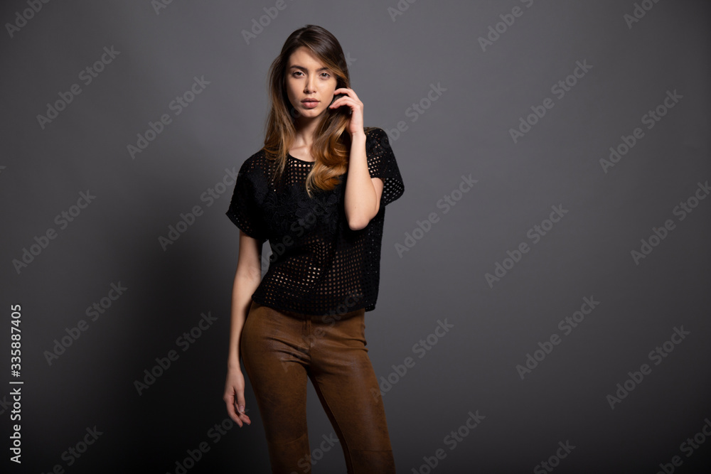 Beautiful people. Model with long hair and natural fresh skin, wear in black shirt and leather pants, looking at camera, over grey background.