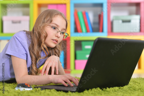 Emotional cute girl using laptop while lying on floor