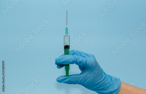 A medic's hand in a blue glove holds a syringe on a blue background