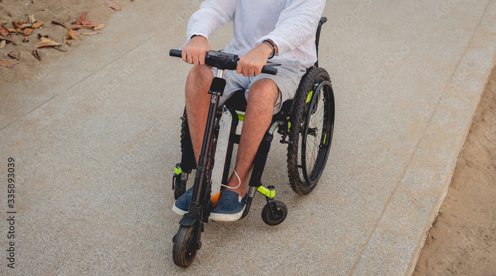 Naklejka premium Disabled man in a wheelchair with electric scooter on the beach