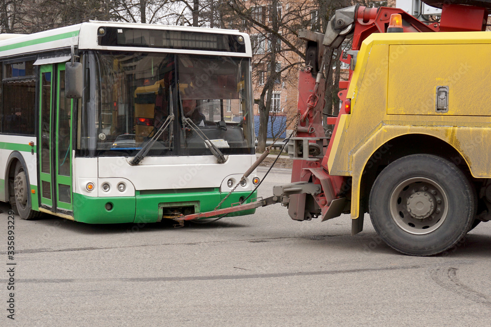 The tractor tows a faulty bus along the city street.