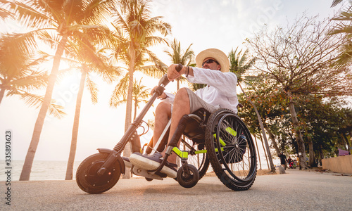 Disabled man in a wheelchair with electric scooter on the beach photo