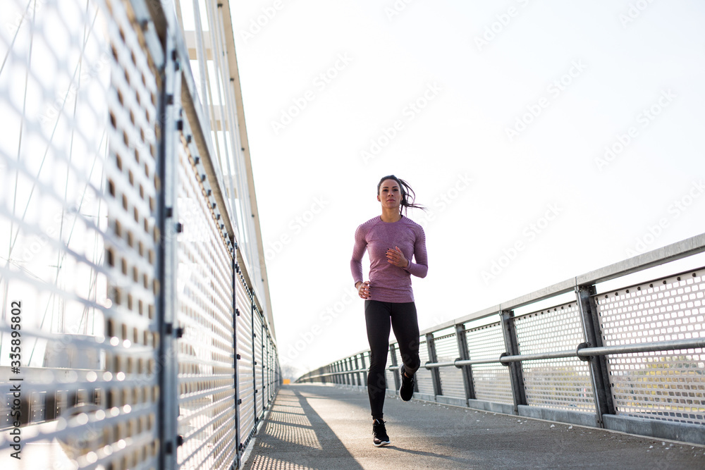 Beautiful fit woman in good shape jogging alone on city bridge.