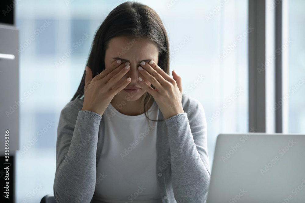 Tired millennial woman sit at desk working at laptop touch massage eyes suffering from blurry vision or dizziness, exhausted young female employee feel unwell having headache or migraine at workplace Tired millennial woman sit at desk working at laptop touch massage eyes suffering from blurry vision or dizziness, exhausted young female employee feel unwell having headache or migraine at workplace