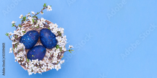Blue easter eggs in a basket with flowers on a blue background. Horizontal photograph. Top view