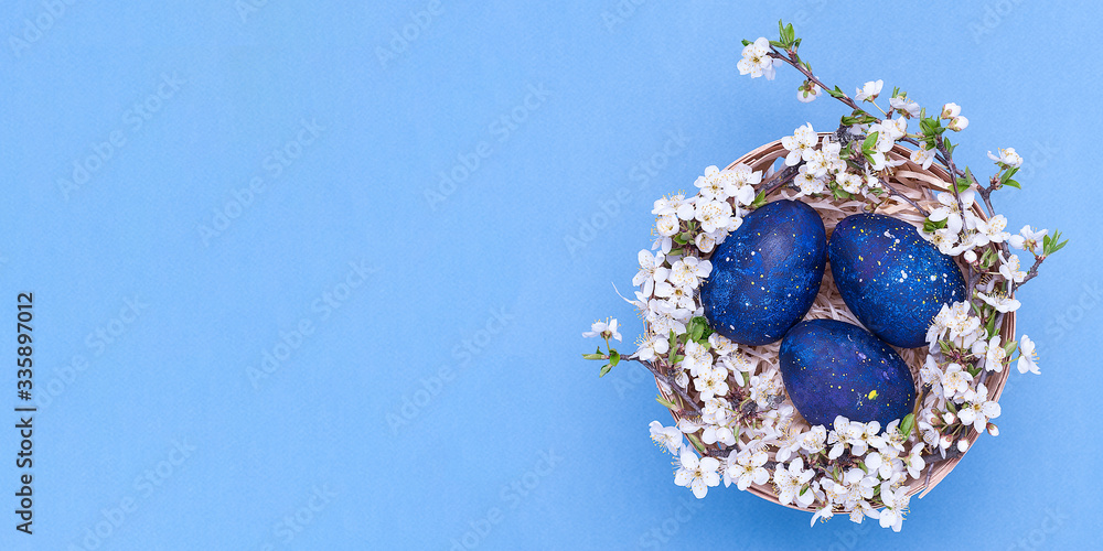 Blue easter eggs in a basket with flowers on a blue background. Horizontal photograph. Top view