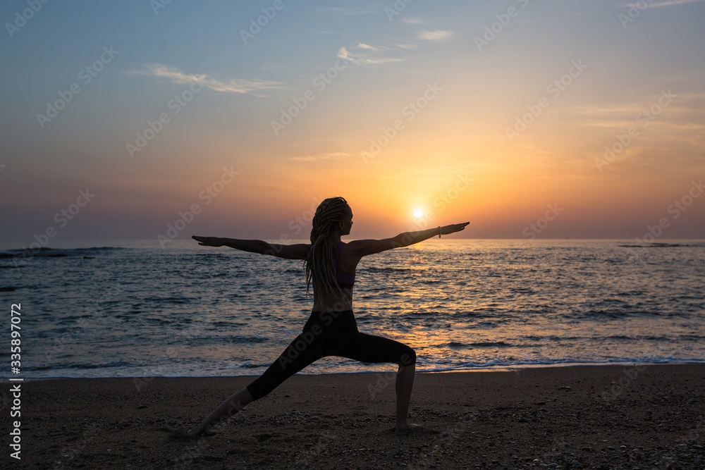 Silhouette of yoga woman, exercises on the ocean beach at evening.