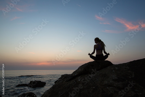 Silhouette of yoga woman on the ocean beach in amazing twilight.