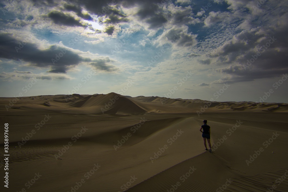 Person walking on sand dune and looking into the distance in the desert of Huacachina, Ica, Peru