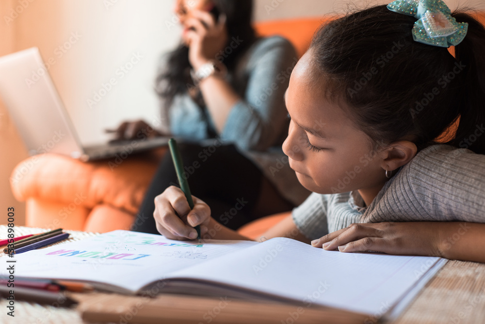 Little girl drawing at home while her mother are talking by smartphone and working on the laptop. Home work concept during virus infection. Little girl drawing at home while her mother are talking by smartphone and working on the laptop. Home work concept during virus infection.