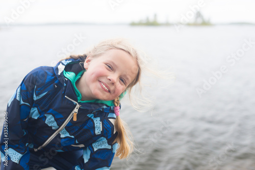Emotion: a girl smiles on the background of the lake. Finnish landscape. Jacket in trend color. Space for text.
