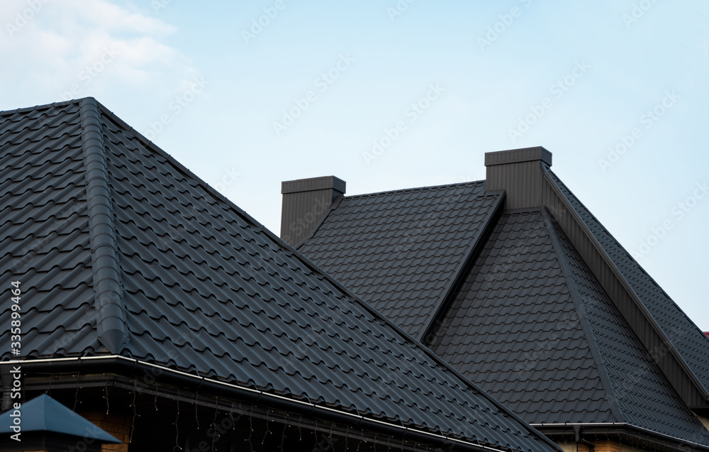 Black metal tile roof. Roof metal sheets. Modern types of roofing materials. Roof of the house, metal roof tile against the blue sky. Building. Black metal tile roof. Roof metal sheets. Modern types of roofing materials. Roof of the house, metal roof tile against the blue sky. Building.