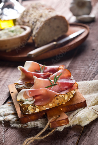 Bruschettas with cream cheese, prosciutto and rosemary on cutting board and wooden table