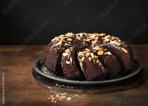 Delicious Homemade Chocolate Bundt Cake with melted chocolate and Sliced Almonds on dark background, copy space. Close up view, horizontal composition, selective focus.