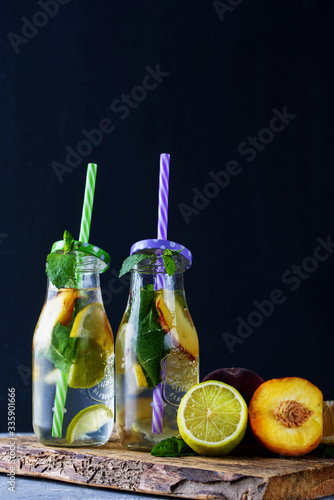 Refreshing fruit drinks with lemon, mint, peach in glass bottles and tubes on the table.