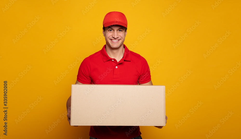 Handsome young happy courier or delivery man in red uniform is posing isolated on yellow background. Handsome young happy courier or delivery man in red uniform is posing isolated on yellow background.