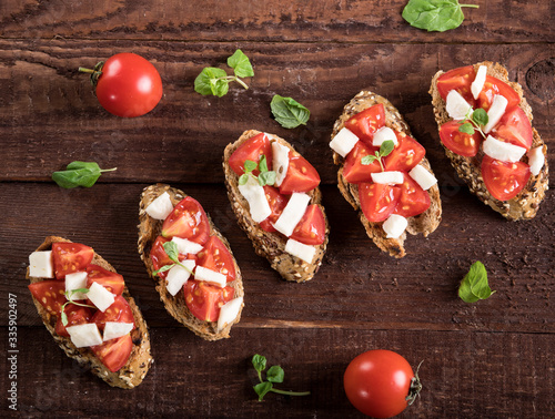 Bruschetta with tomatoes, mozzarella cheese and basil on wooden background. Top view