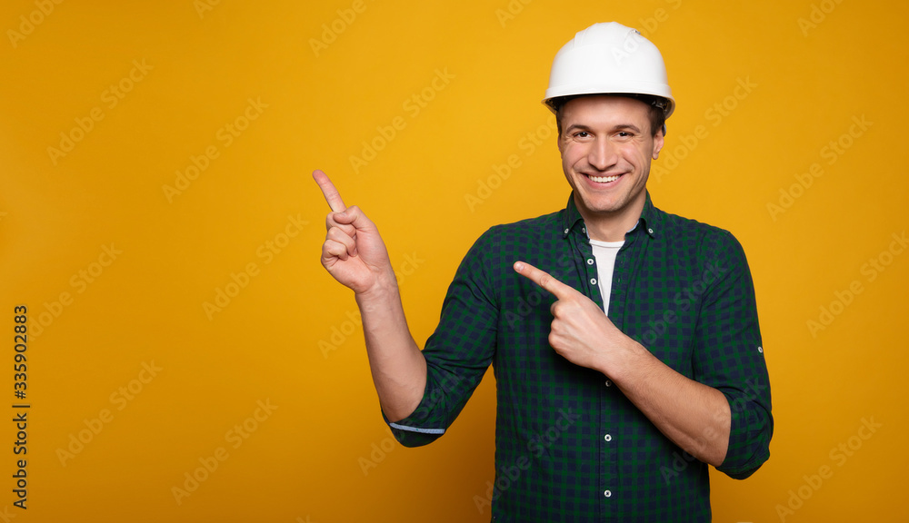Close up photo of young happy and confident foreman or architect in build helmet is posing isolated on yellow background.