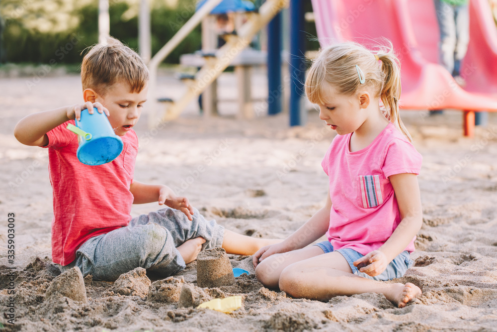 Two Caucasian children sitting in sandbox playing with beach toys. Little girl and boy friends having fun together on a playground. Summer outdoor activity for kids. Leisure time lifestyle childhood. Two Caucasian children sitting in sandbox playing with beach toys. Little girl and boy friends having fun together on a playground. Summer outdoor activity for kids. Leisure time lifestyle childhood.