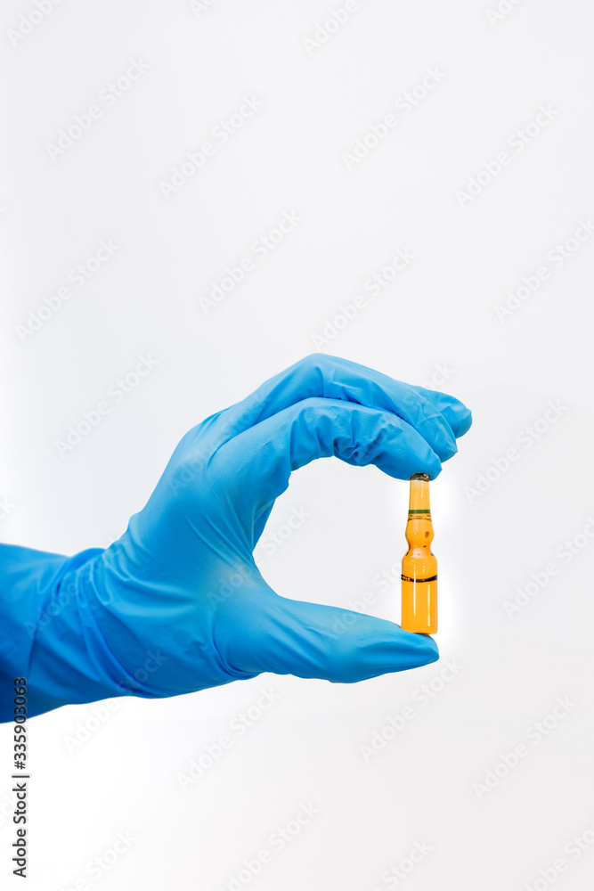 hand in a blue medical glove holds a glass ampoule with medicines on a white background, the doctor prepares an injection for the patient, the introduction of a vaccine hand in a blue medical glove holds a glass ampoule with medicines on a white background, the doctor prepares an injection for the patient, the introduction of a vaccine
