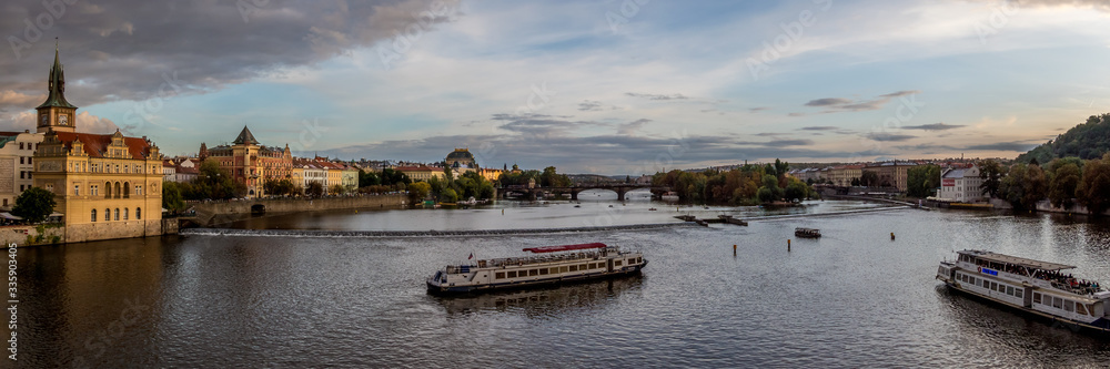 Panoramic view of the Vltava River across to the national Theatre, with tourist boats crossing the river