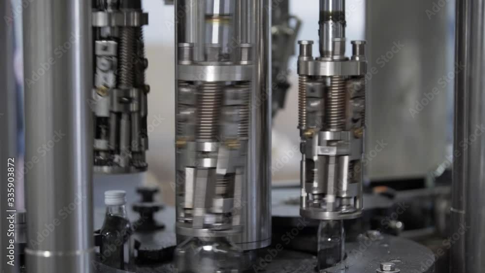 Automatic machine screwing cap on bottle with alcoholic beverages. Spill of vodka in glass bottles at distillery. Production process of alcoholic beverages in modern factory. Automatic machine screwing cap on bottle with alcoholic beverages. Spill of vodka in glass bottles at distillery. Production process of alcoholic beverages in modern factory.