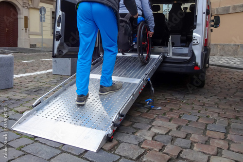 Billede på lærred Assistant helping disabled person on wheelchair with transport using accessible