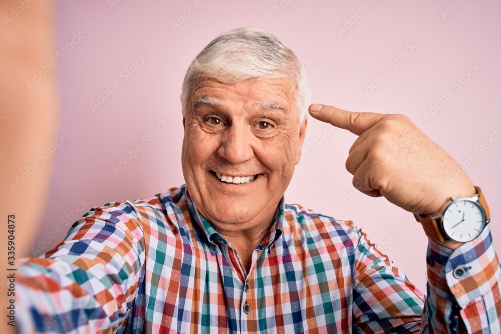 Senior handsome hoary man wearing casual shirt making selfie by the camera very happy pointing with hand and finger Senior handsome hoary man wearing casual shirt making selfie by the camera very happy pointing with hand and finger