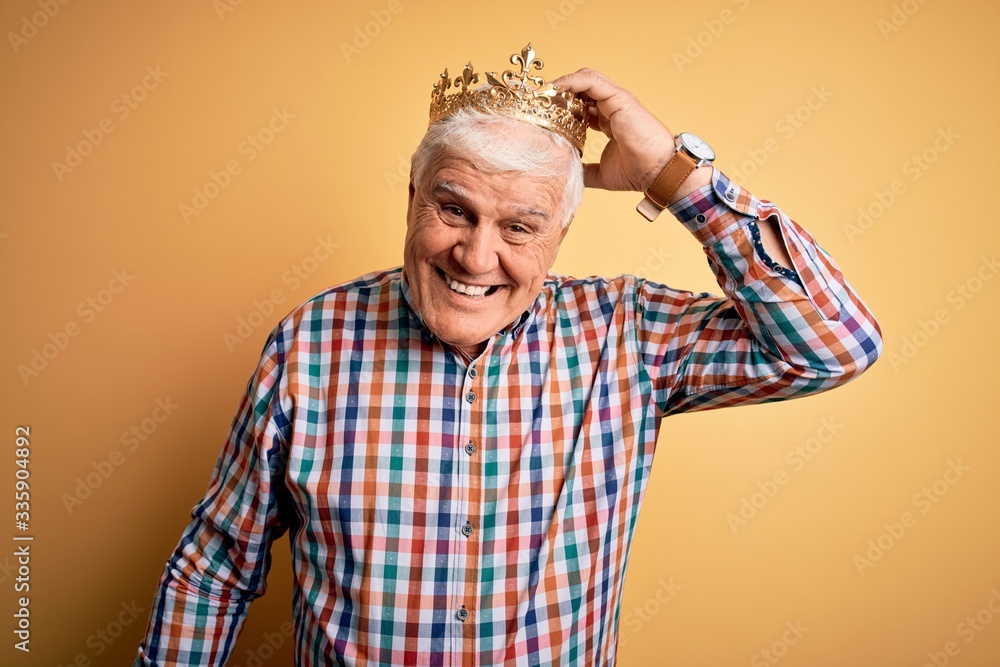 Senior handsome hoary man wearing golden crown of king over isolated yellow background confuse and wonder about question. Uncertain with doubt, thinking with hand on head. Pensive concept. Senior handsome hoary man wearing golden crown of king over isolated yellow background confuse and wonder about question. Uncertain with doubt, thinking with hand on head. Pensive concept.